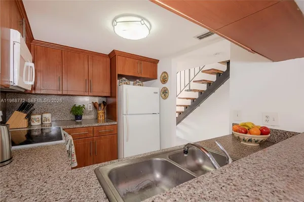 a kitchen with stainless steel appliances granite countertop a sink a refrigerator and a white cabinets