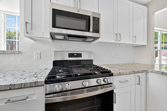 a kitchen with stainless steel appliances granite countertop white cabinets and a stove top oven
