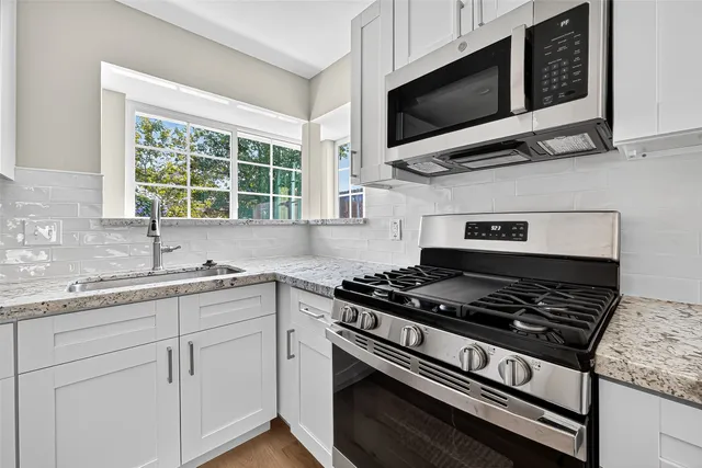 a kitchen with stainless steel appliances white cabinets granite counter tops and a window