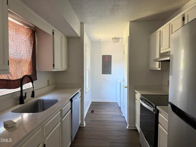 a kitchen with stainless steel appliances a sink dishwasher a refrigerator a stove and white cabinets with wooden floor