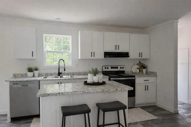 a kitchen with granite countertop a stove a sink dishwasher and white cabinets with wooden floor