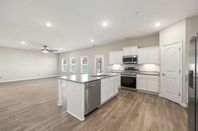 a kitchen with stainless steel appliances granite countertop a stove top oven a sink dishwasher and a refrigerator with wooden floor