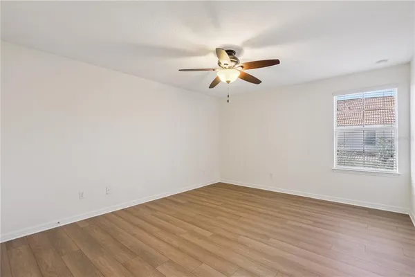 an empty room with wooden floor fan and windows