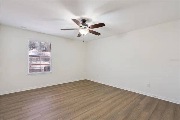 an empty room with wooden floor ceiling fan and window