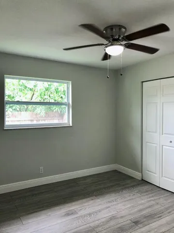 an empty room with wooden floor fan and windows
