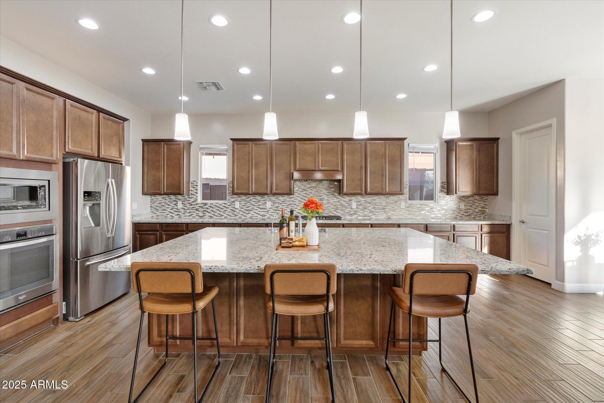 9275 West Plum Road Peoria, AZ 85383 - Photo 7 of 39 a kitchen with stainless steel appliances granite countertop a kitchen island hardwood floor and chairs