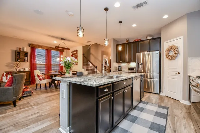 a kitchen with stainless steel appliances granite countertop a sink a stove a refrigerator and island with wooden floor