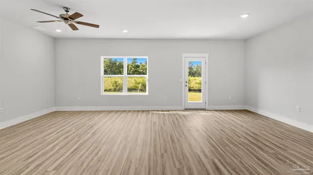 an empty room with wooden floor ceiling fan and windows