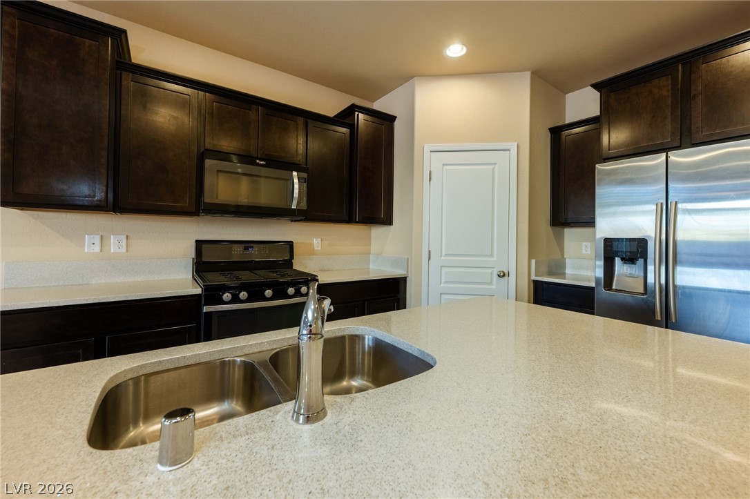 11016 Prairie Grove Road Las Vegas, NV 89179 - Photo 7 of 37 A well-appointed kitchen features dark wood cabinetry, light countertops, and modern stainless-steel appliances.