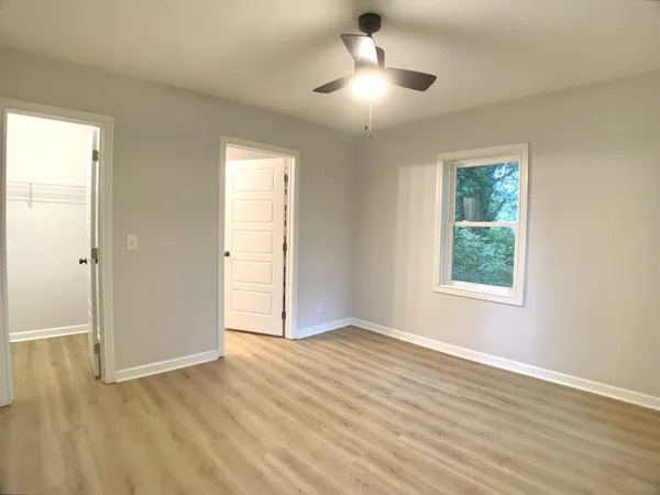 an empty room with wooden floor chandelier fan and windows
