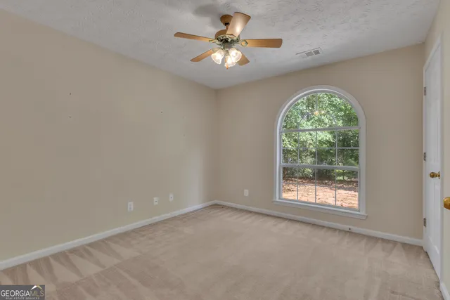 an empty room with a chandelier fan and windows