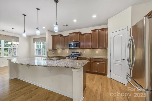 a kitchen with stainless steel appliances granite countertop a refrigerator a sink a stove and a wooden floors