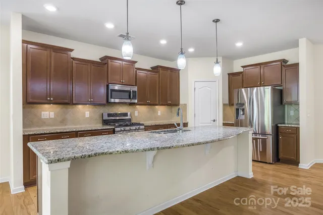 a kitchen with stainless steel appliances granite countertop a refrigerator a sink a stove and a refrigerator