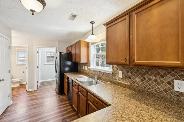 a kitchen with stainless steel appliances granite countertop a stove top oven a refrigerator a sink and dishwasher with wooden floor