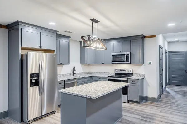 a large kitchen with stainless steel appliances a large counter top a sink a refrigerator and wooden floors