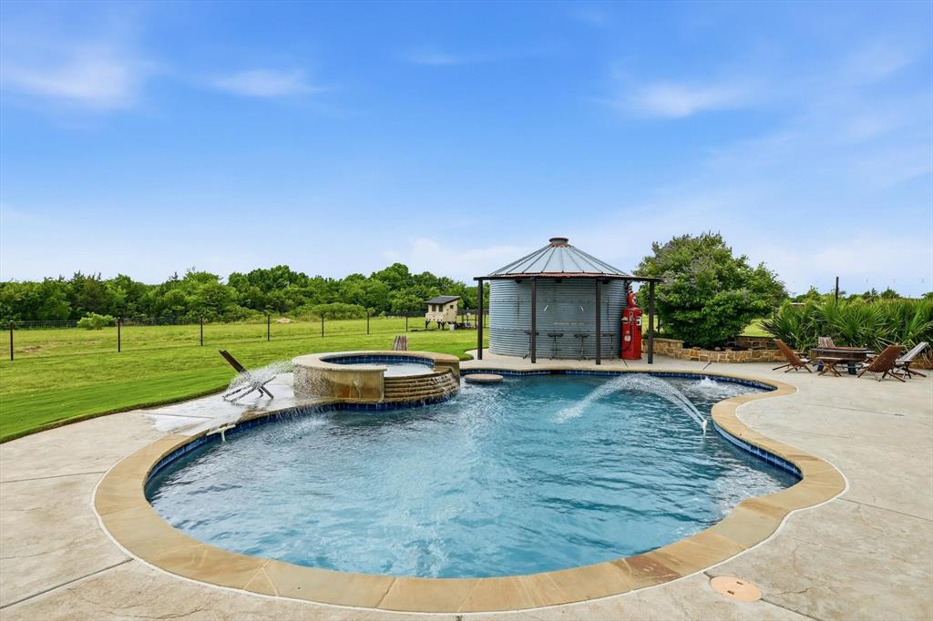 6020 Honeysuckle Road Midlothian, TX 76065 - Photo 28 of 39 Curved swimming pool with integrated spa and water features, surrounded by a stamped concrete patio with stone coping