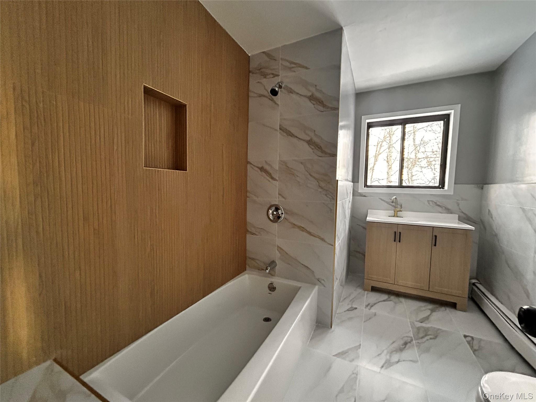 218 Beattie Road Washingtonville, NY 10992 - Photo 10 of 15 Bathroom featuring vanity, tile walls, washtub / shower combination, light marble finish flooring, and a wainscoted wall