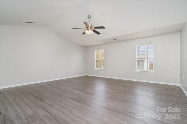 an empty room with wooden floor ceiling fan and windows