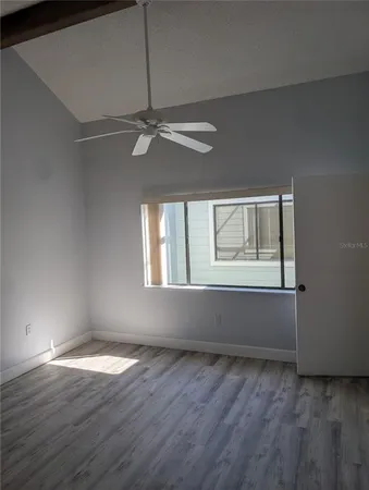 an empty room with wooden floor fan and windows
