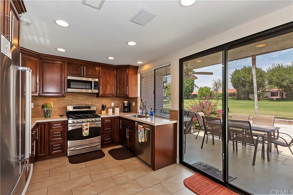 109 Torremolinos Drive Rancho Mirage, CA 92270 - Photo 13 of 33 a kitchen with stainless steel appliances granite countertop a stove top oven a sink dishwasher a dining table and chairs with wooden floor
