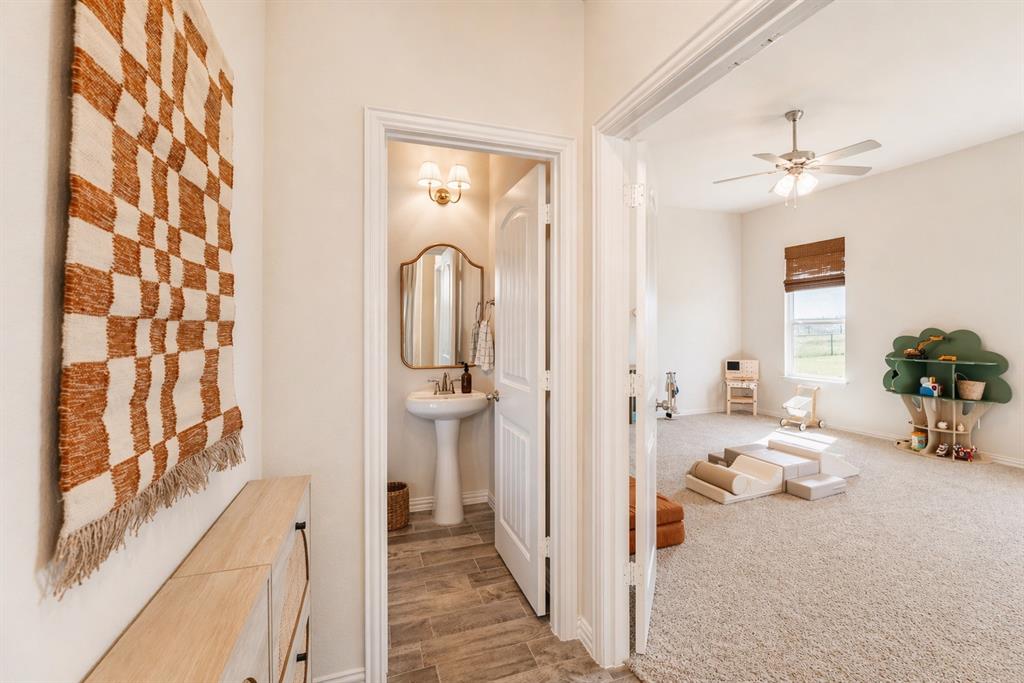 1530 County Road 200 Valley View, TX 76272 - Photo 18 of 34 Conveniently located powder room featuring a pedestal sink, framed mirror, and warm-toned wall sconce, with wood-finish flooring