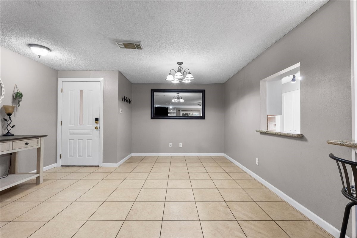883 Silverpines Road Houston, TX 77062 - Photo 5 of 38 This room features a neutral color palette with beige tile flooring and soft gray walls. It includes a ceiling light fixture, a wall mirror, and a small pass-through window to the kitchen, providing an open feel. The entry area is adjacent, offering a welcoming space.