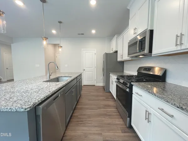 a kitchen with kitchen island granite countertop a refrigerator a sink a center island and wooden floor