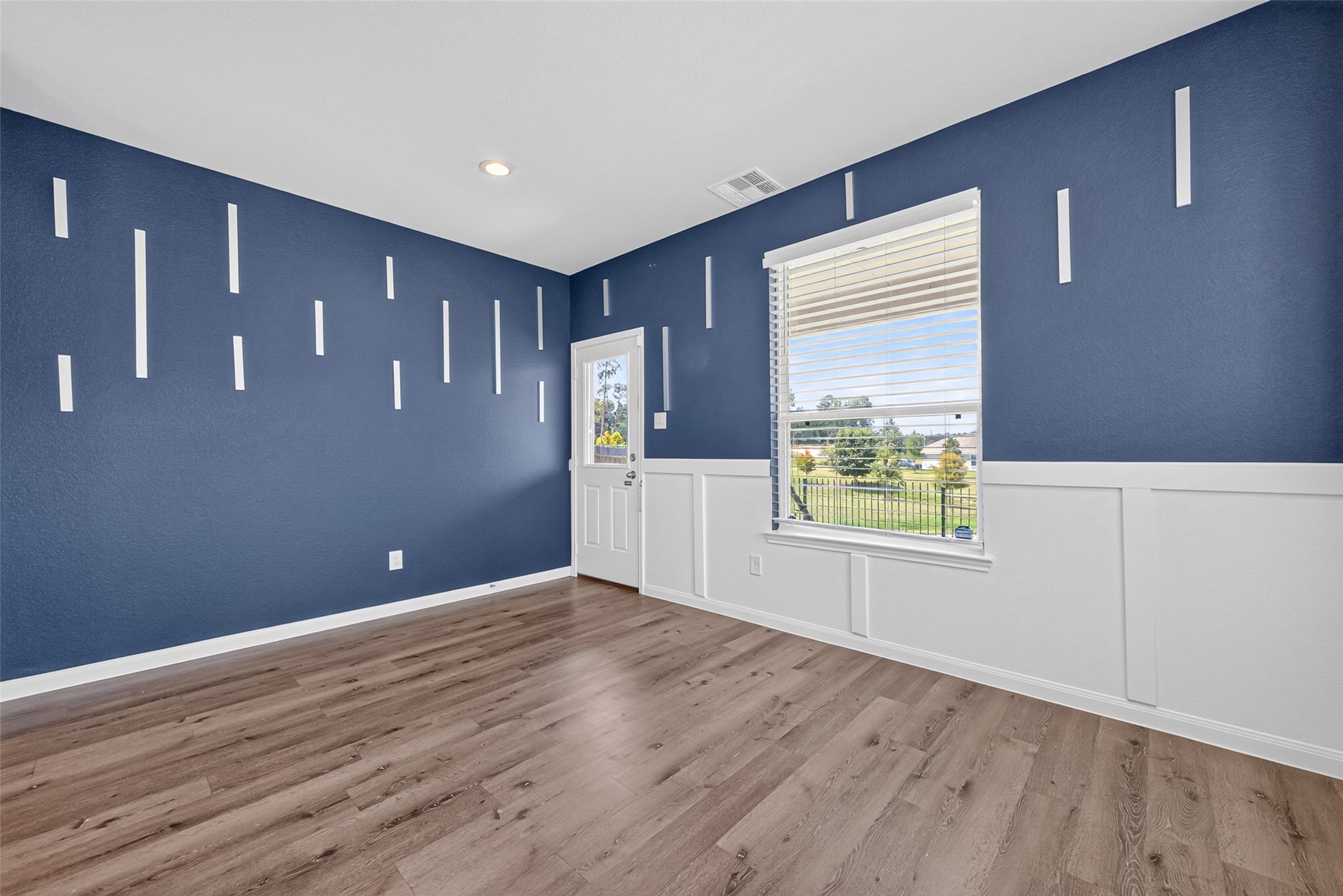 2526 Sturgeon Way Conroe, TX 77384 - Photo 14 of 49 This room features elegant blue walls with white geometric accents, complemented by light brown wood flooring. It includes a large window with blinds offering natural light and a view of a fenced yard, along with a door for outdoor access. Perfect for a stylish and functional space.