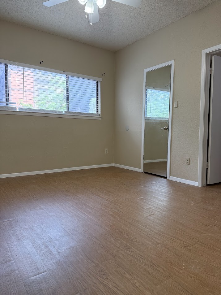 806 West 24th Street, Unit 223 Austin, TX 78705 - Photo 11 of 16 Empty room with wood finished floors, a textured ceiling, a ceiling fan, and baseboards