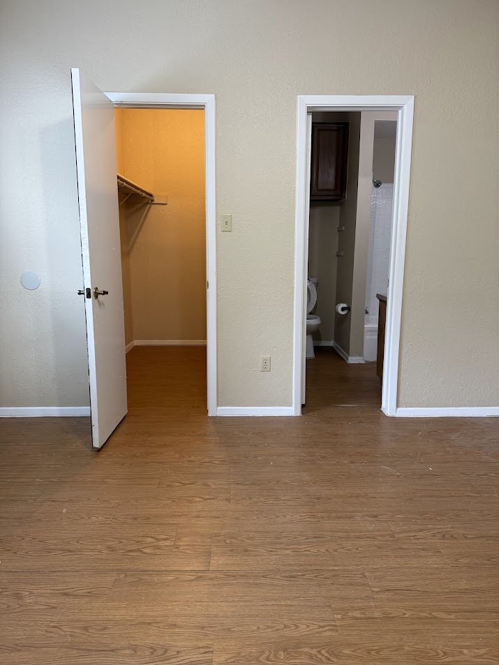 806 West 24th Street, Unit 223 Austin, TX 78705 - Photo 13 of 16 Unfurnished bedroom featuring wood finished floors, a walk in closet, a closet, baseboards, and ensuite bathroom