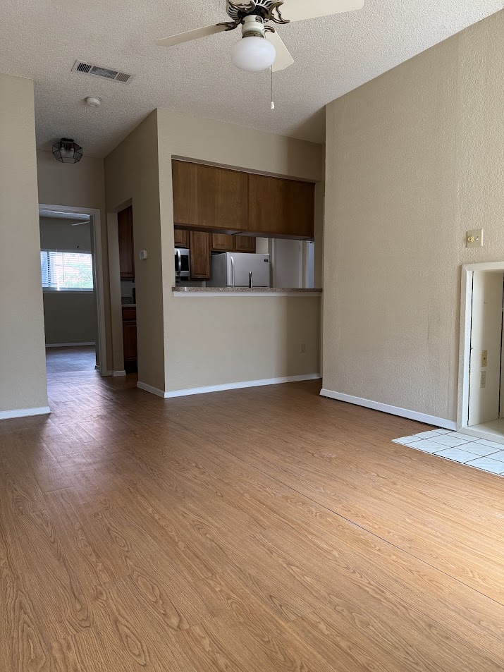 806 West 24th Street, Unit 223 Austin, TX 78705 - Photo 2 of 16 Unfurnished living room featuring a textured ceiling, visible vents, baseboards, wood finished floors, and ceiling fan