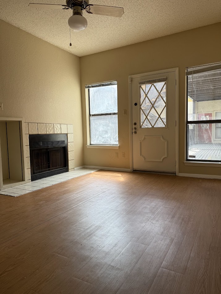 806 West 24th Street, Unit 223 Austin, TX 78705 - Photo 3 of 16 Unfurnished living room featuring a ceiling fan, wood finished floors, a tile fireplace, and a textured ceiling