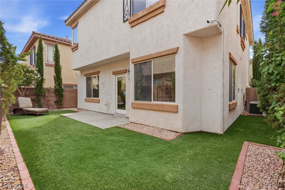 8932 Caledon Ridge Court Las Vegas, NV 89149 - Photo 36 of 39 Manicured green turf surrounds a concrete patio alongside the textured stucco exterior.