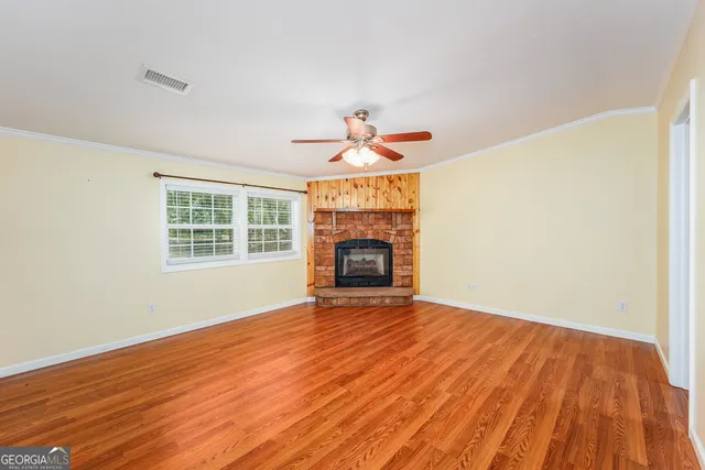 a view of an empty room with wooden floor fireplace and a window