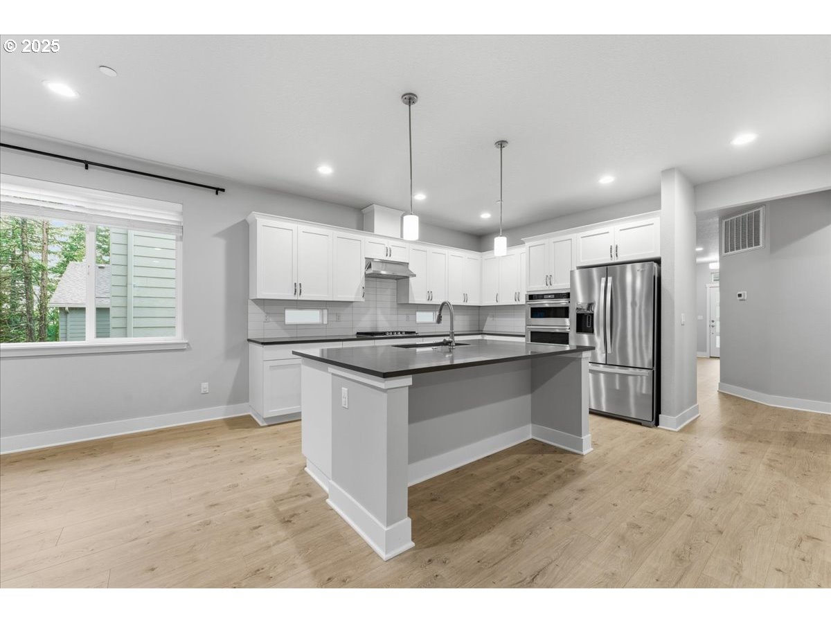 8565 Southwest 176th Avenue Beaverton, OR 97007 - Photo 5 of 39 a kitchen with stainless steel appliances kitchen island granite countertop a refrigerator a sink a stove and a wooden floors