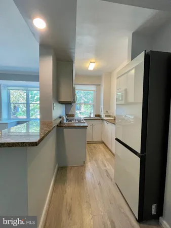 a large kitchen with a refrigerator a sink dishwasher a stove and white cabinets with wooden floor