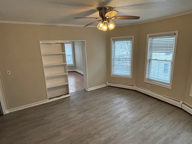 an empty room with wooden floor fan and windows