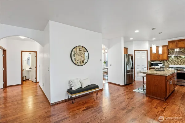 a living room with stainless steel appliances kitchen island granite countertop a refrigerator a stove and a wooden floors