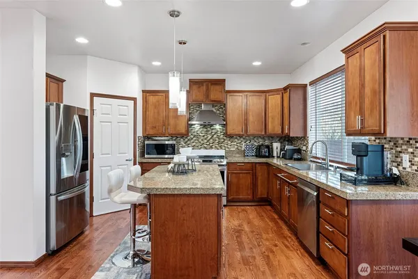 a kitchen with stainless steel appliances granite countertop a refrigerator a sink dishwasher a stove with wooden cabinets and floor