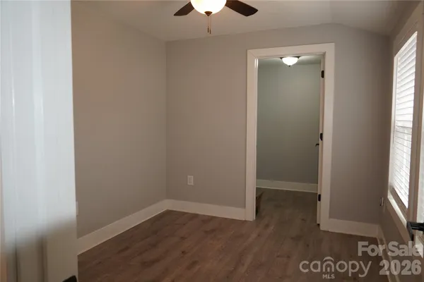 an empty room with wooden floor chandelier fan and windows