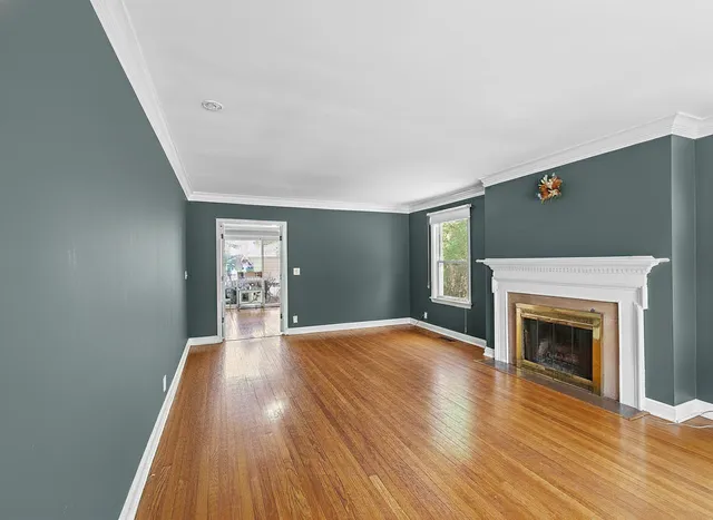 a view of an empty room with wooden floor fireplace and a window