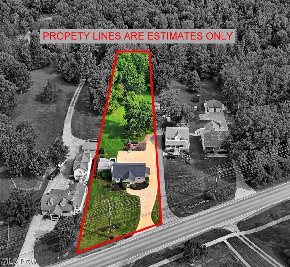 Property with a paved driveway, a large lawn, and mature trees