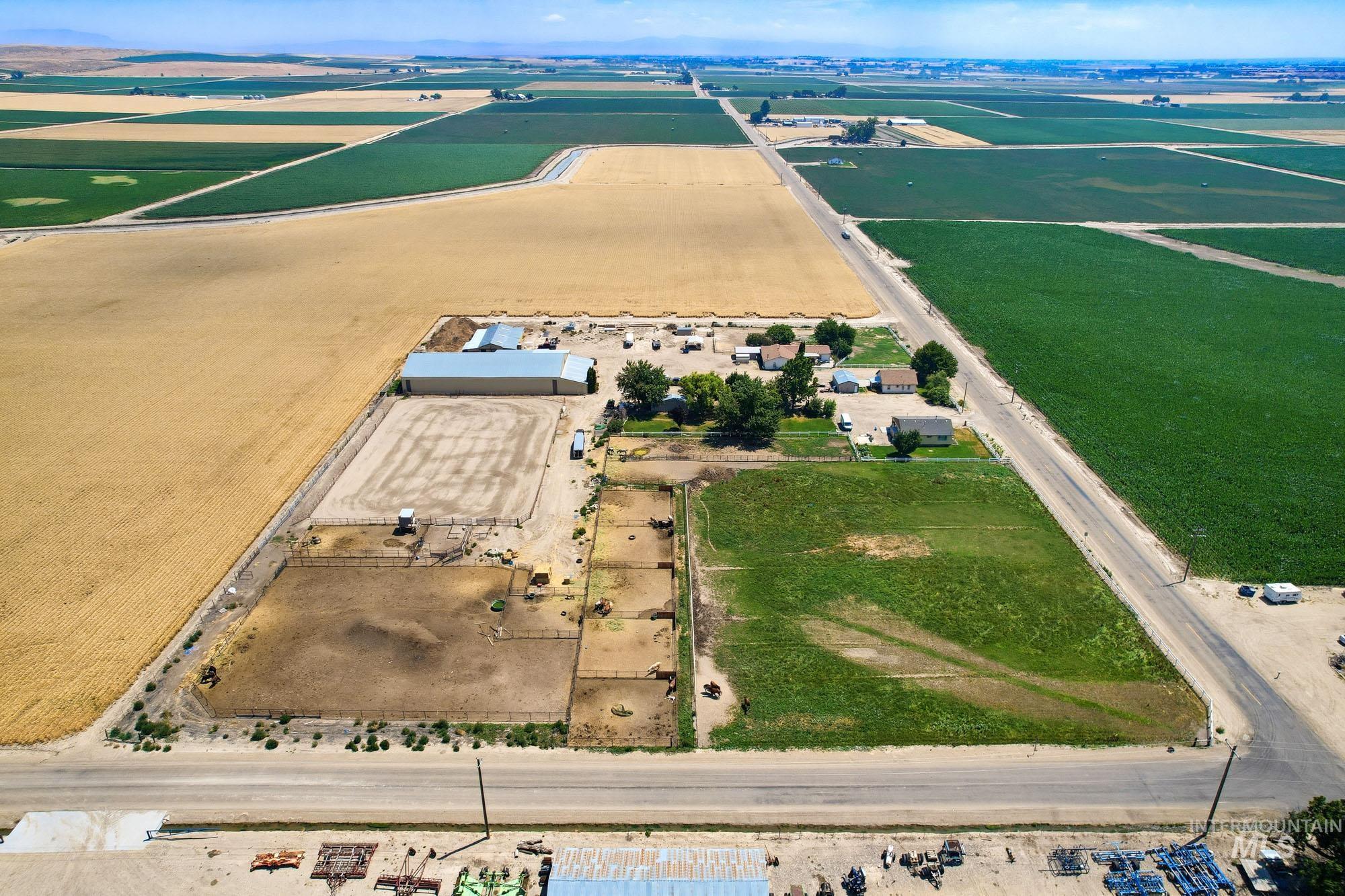 24900 Market Road Parma, ID 83660 - Photo 32 of 50 Expansive property featuring multiple agricultural fields, a large metal-roofed outbuilding, a fenced riding arena, and several smaller fenced paddocks