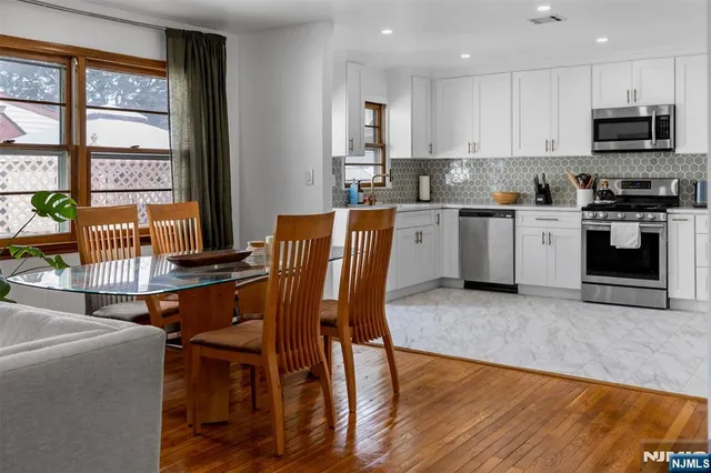 a kitchen with stainless steel appliances granite countertop a stove top oven a sink a dining table and chairs with wooden floor