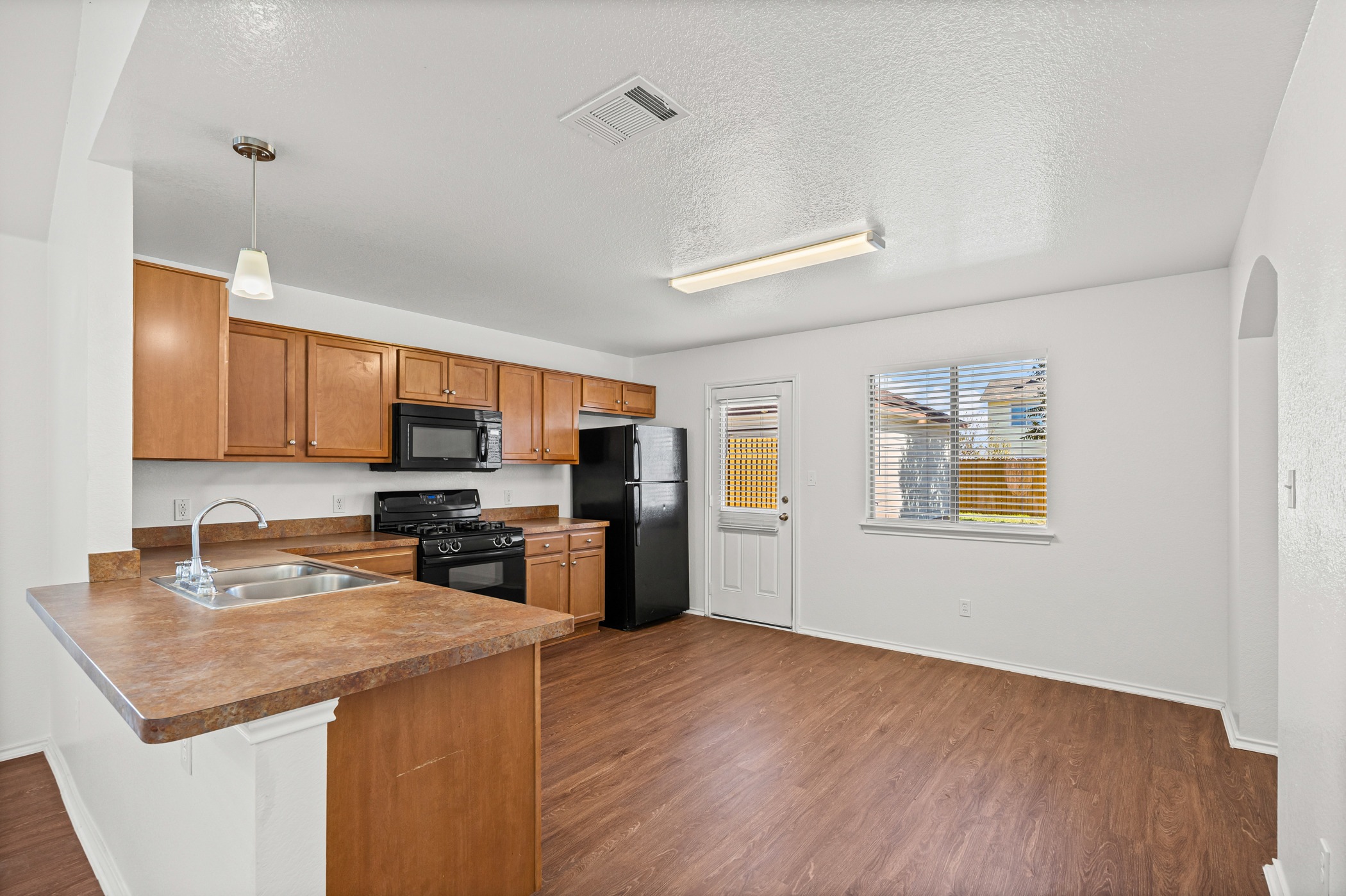 4503 Halliday Avenue Austin, TX 78725 - Photo 8 of 21 Kitchen with brown cabinets, dark wood-style floors, pendant lighting, black appliances, and a peninsula