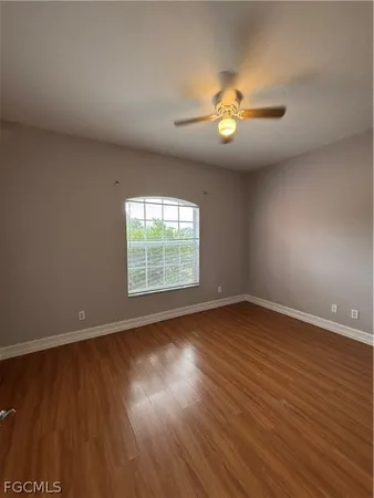 an empty room with wooden floor chandelier fan and windows
