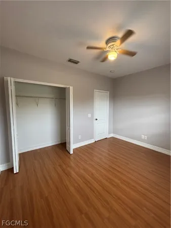 a view of an empty room with wooden floor and a ceiling fan
