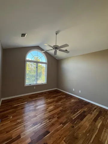 an empty room with wooden floor chandelier fan and windows