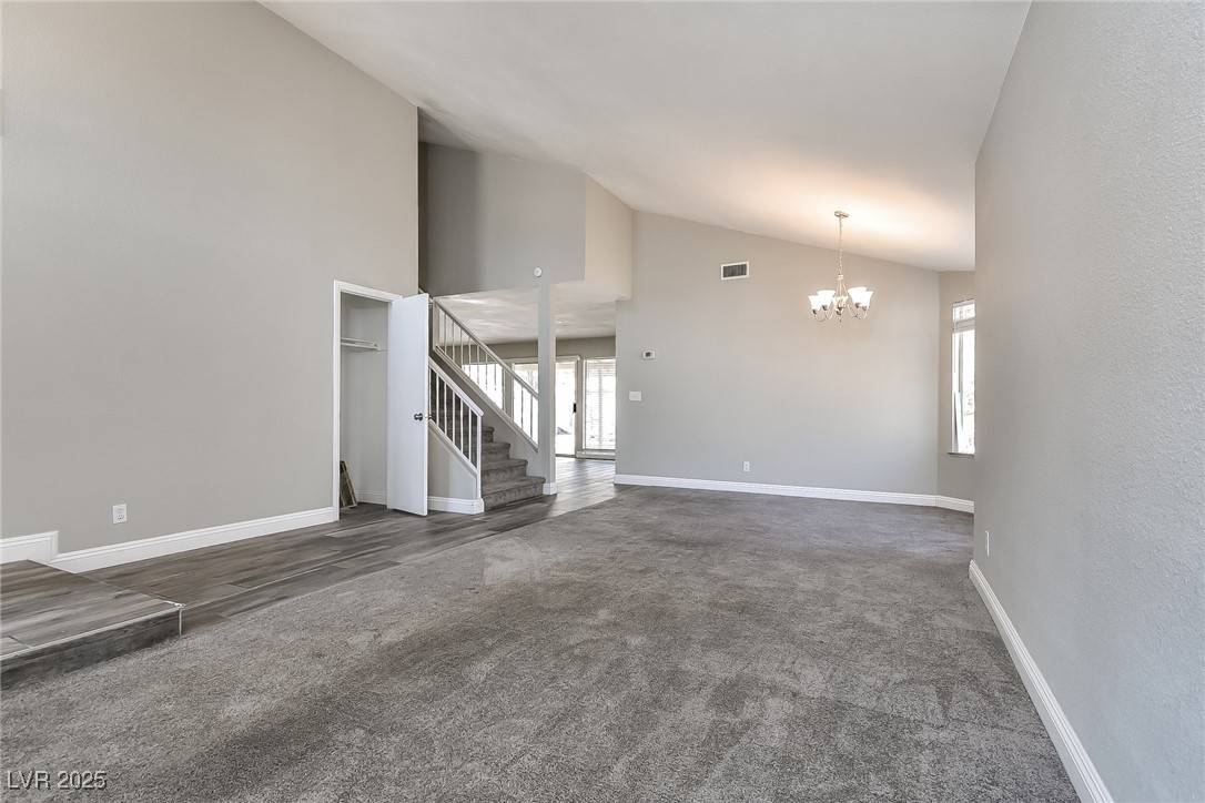 741 Round Table Drive Las Vegas, NV 89110 - Photo 6 of 22 Unfurnished living room with carpet floors, high vaulted ceiling, a chandelier, and stairs