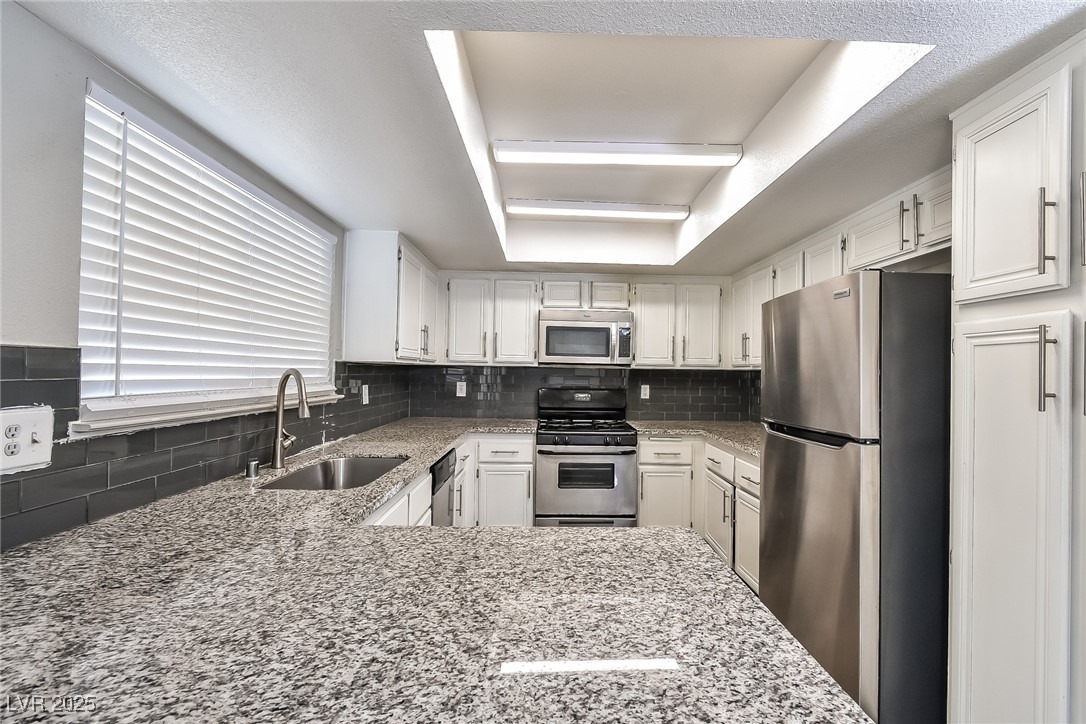 741 Round Table Drive Las Vegas, NV 89110 - Photo 7 of 22 Kitchen featuring a tray ceiling, appliances with stainless steel finishes, tasteful backsplash, light stone counters, and white cabinets